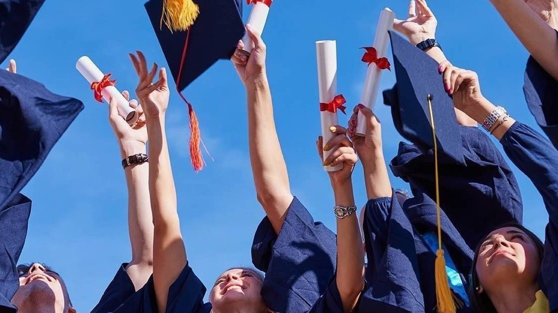 Graduates in caps and gowns raising diplomas against a blue sky