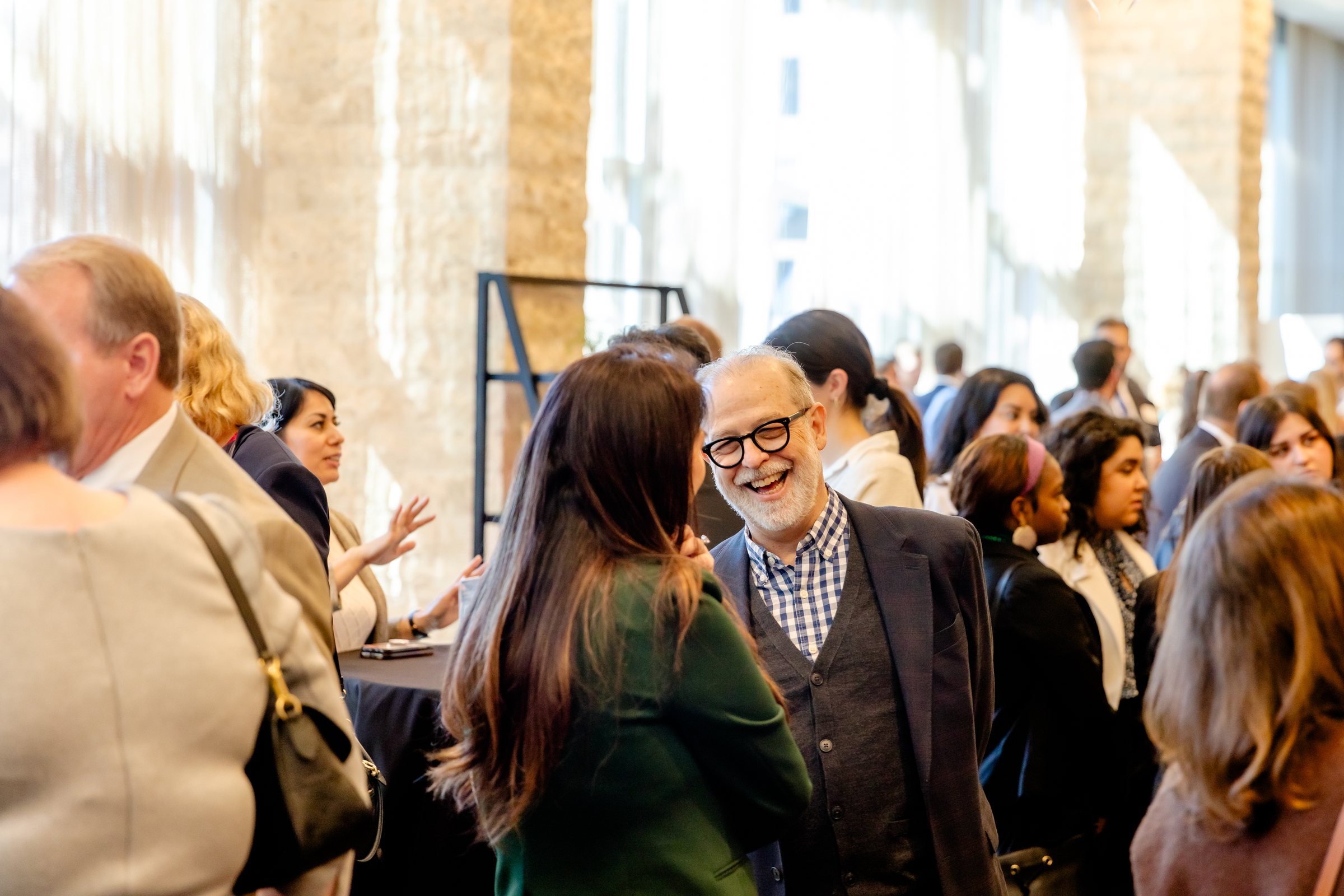 A crowded reception in a bright hall, two guests laughing in conversation